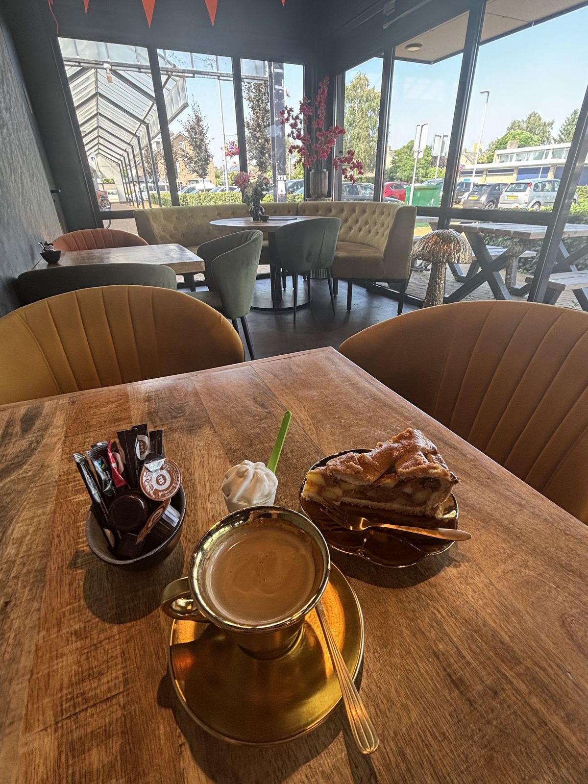 Glas koffie met slagroom en een stuk appeltaart aan tafel bij het raam